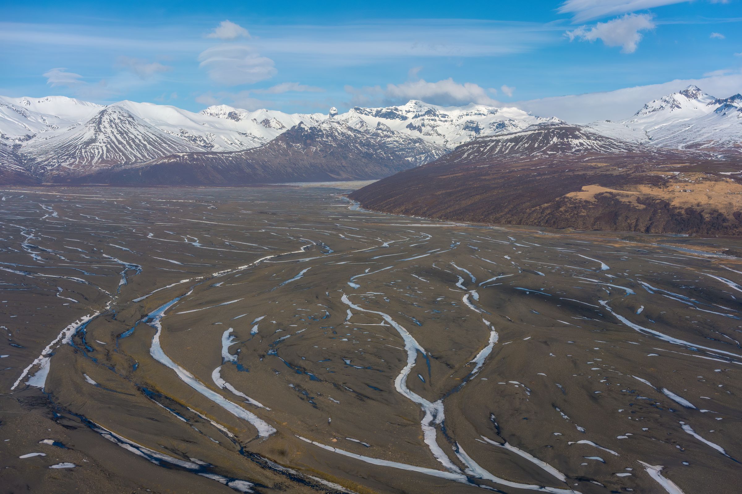 an aerial view of a river flowing through a valley surrounded by snow covered mountains