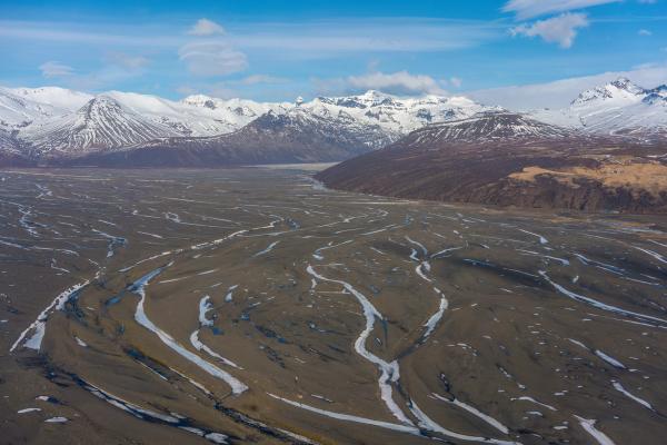 an aerial view of a river flowing through a valley surrounded by snow covered mountains