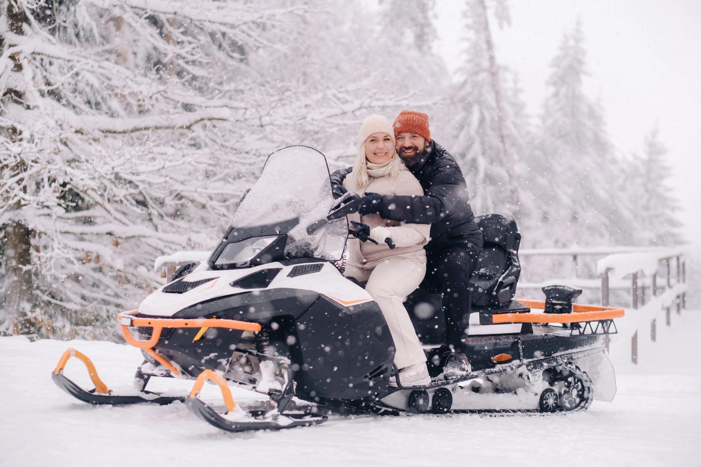 a man and a woman are sitting on a snowmobile in the snow .