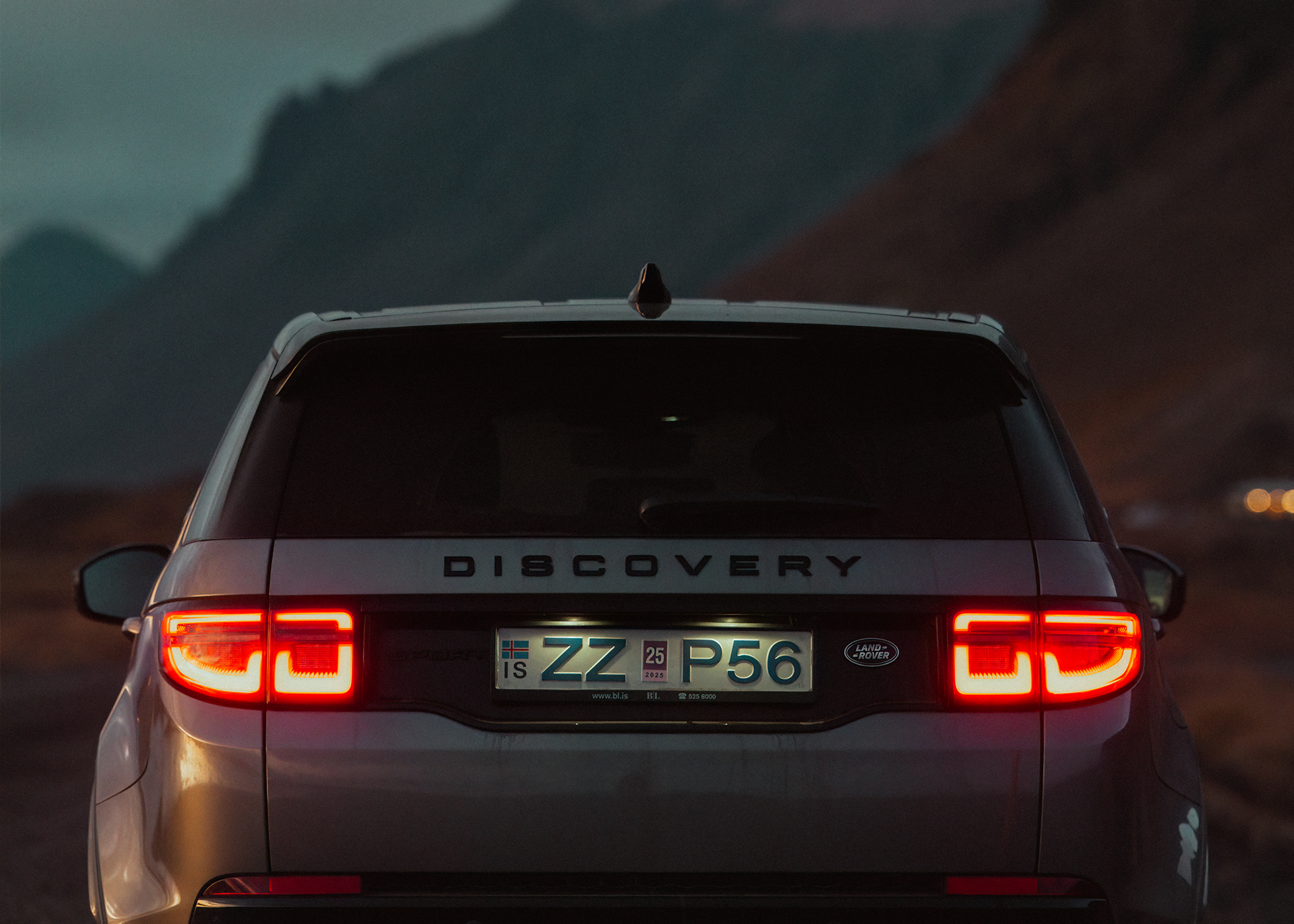 Heckansicht eines Land Rover Discovery Sport 4x4 mit eingeschalteten Rückleuchten vor einer Bergkulisse