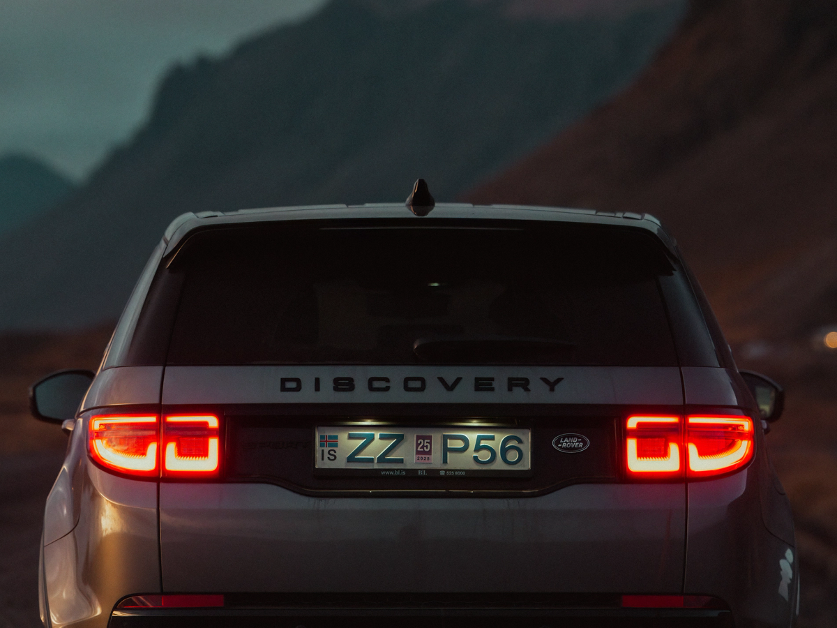 Discovery Sport – Ansicht der Rückleuchten Heckansicht eines Land Rover Discovery Sport 4x4 mit eingeschalteten Rückleuchten vor einer Bergkulisse