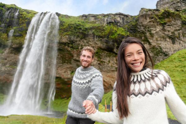 una pareja con jerseys típicos islandeses con una cascada al fondo