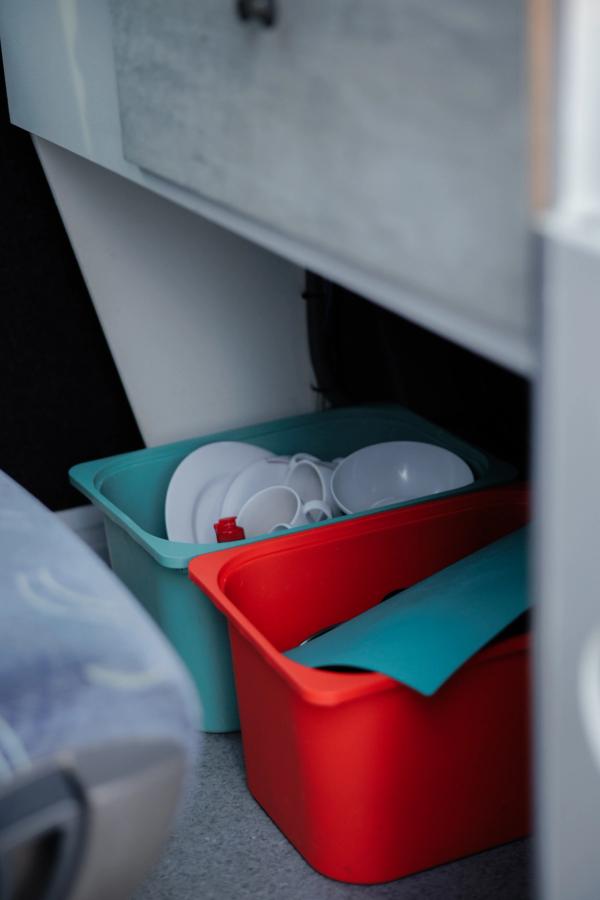 Boxen mit Tellern und eine Schneidematte unter der Küchenzeile in einem großen Camper für fünf Personen
