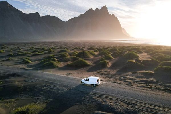 an aerial view of a white van driving down a dirt road in the desert .