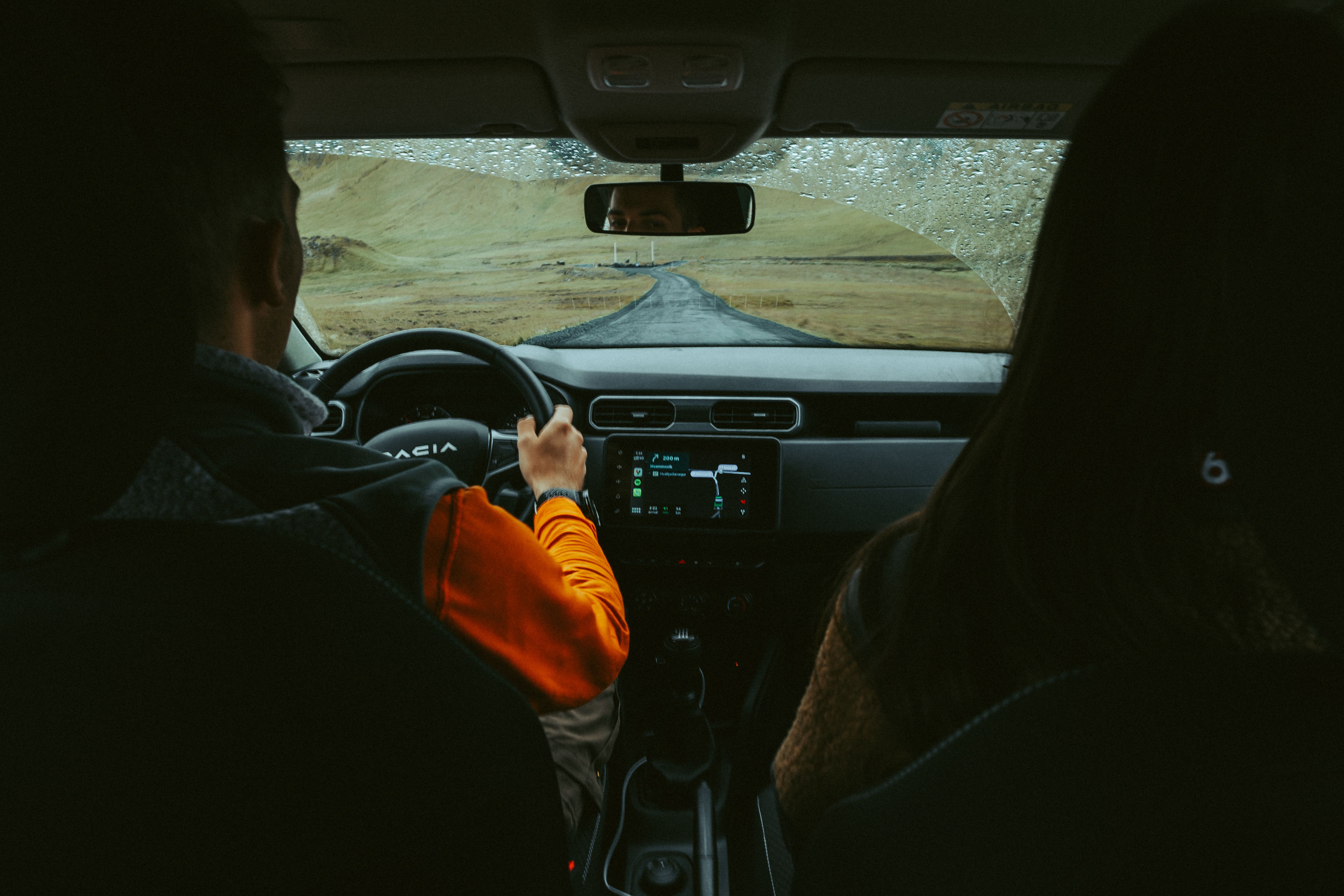 Driver and passenger seen from the rear seat on a paved road through open hills
