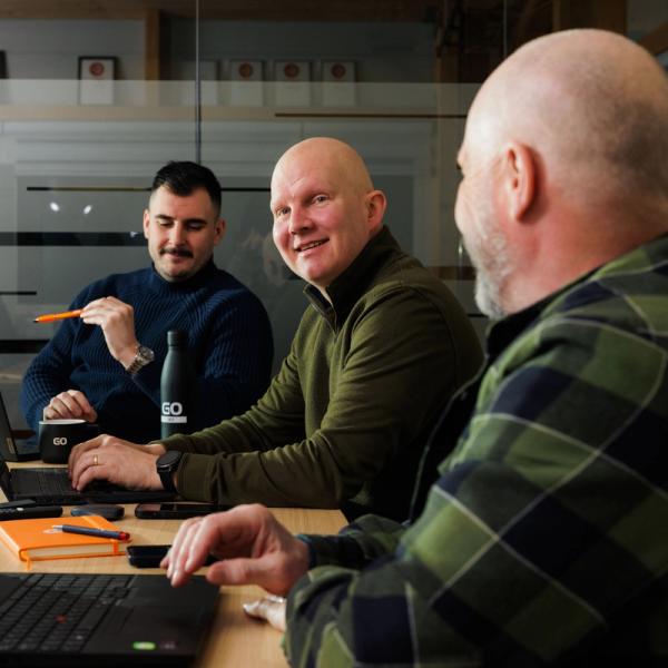 a group of men are sitting at a table with laptops .