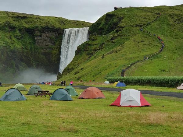 tents in a grass field with a waterfall on the background