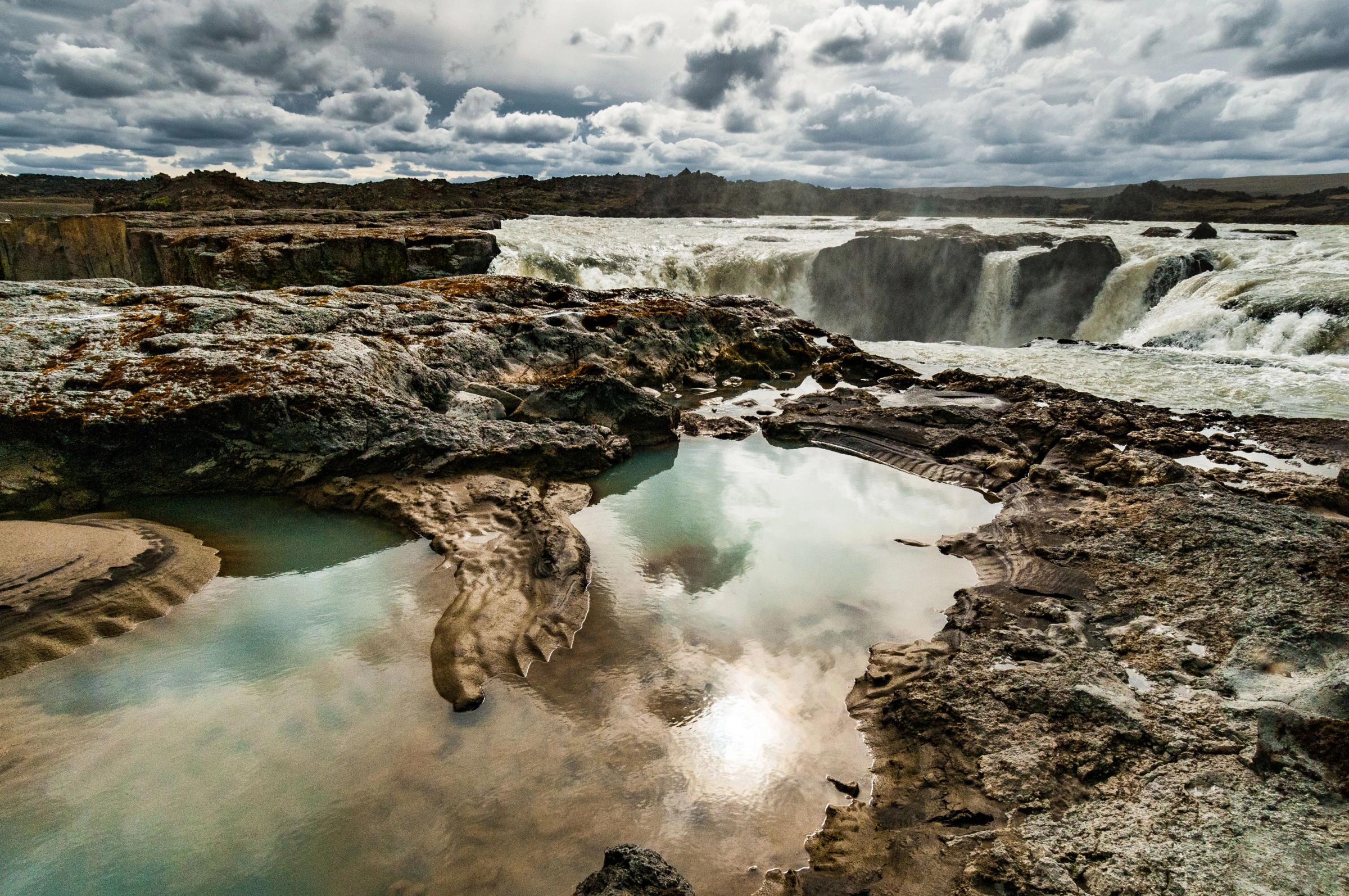 a waterfall is reflected in a pool of water surrounded by rocks .