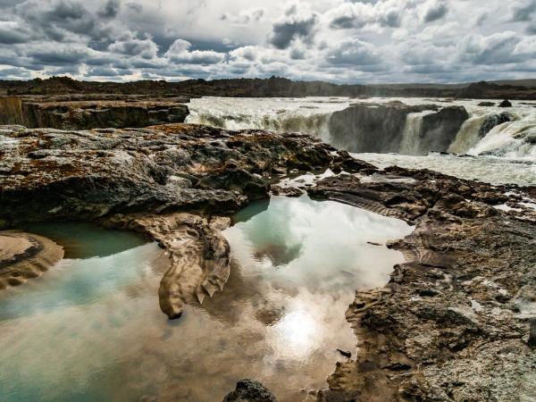 a waterfall is reflected in a pool of water surrounded by rocks .
