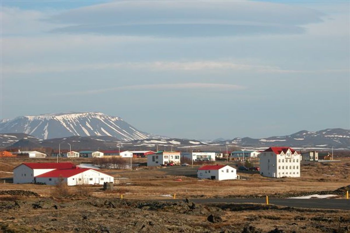 Un pueblo de casas blancas con tejados rojos en un paisaje rocoso, con montañas nevadas al fondo.