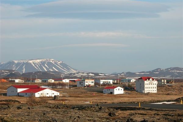A village with white buildings and red roofs in a rocky landscape, with snow-capped mountains in the background.