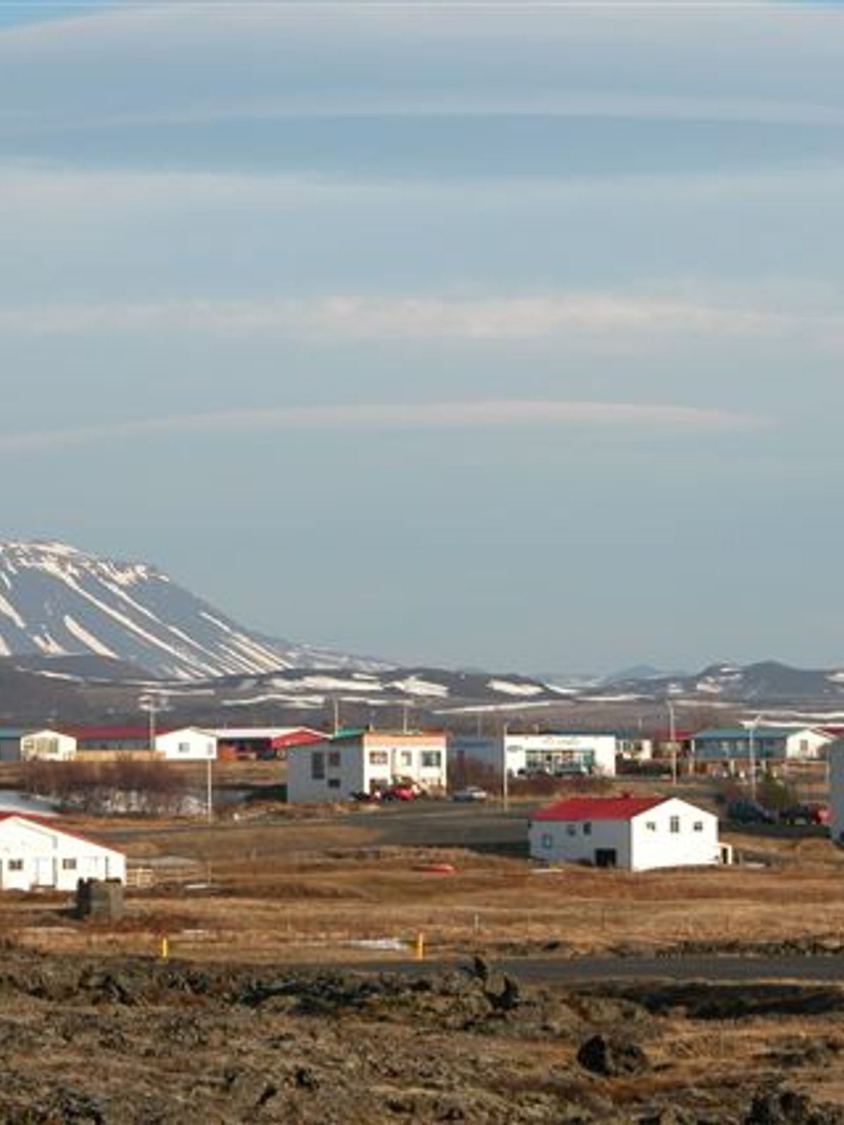 Un pueblo de casas blancas con tejados rojos en un paisaje rocoso, con montañas nevadas al fondo.