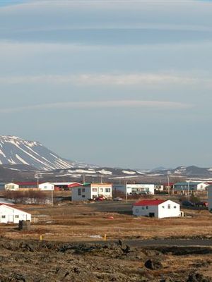 A village with white buildings and red roofs in a rocky landscape, with snow-capped mountains in the background.