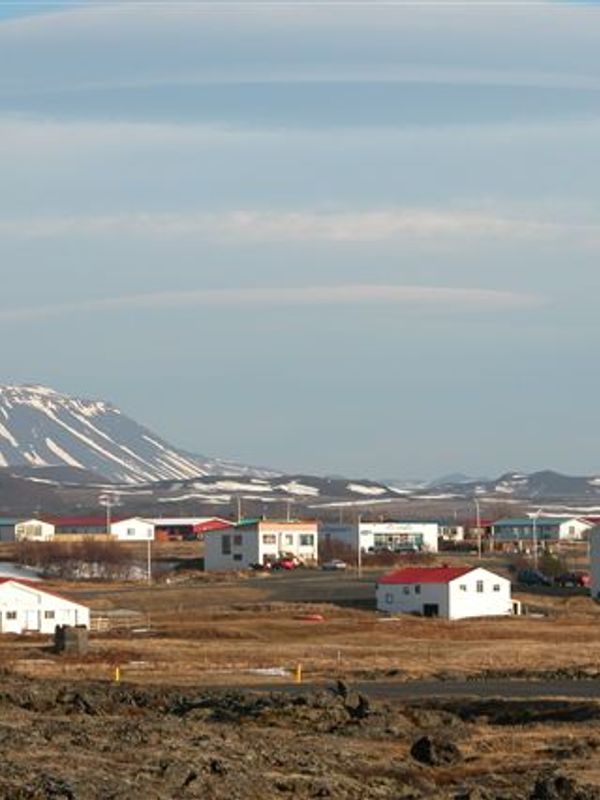A village with white buildings and red roofs in a rocky landscape, with snow-capped mountains in the background.