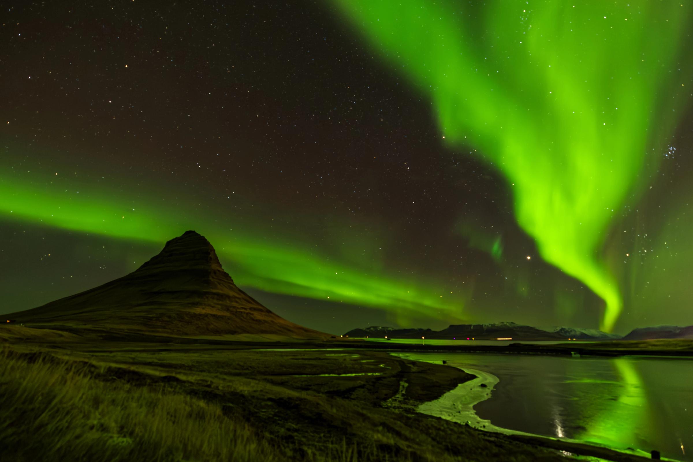 la aurora boreal brilla sobre una montaña y un lago.