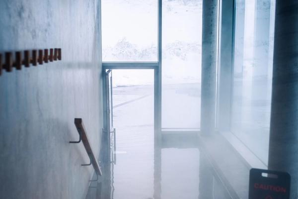Steamy indoor area with a wet floor caution sign, overlooking a snowy outdoor landscape.