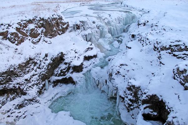 una cascada congelada rodeada de rocas y acantilados cubiertos de nieve.