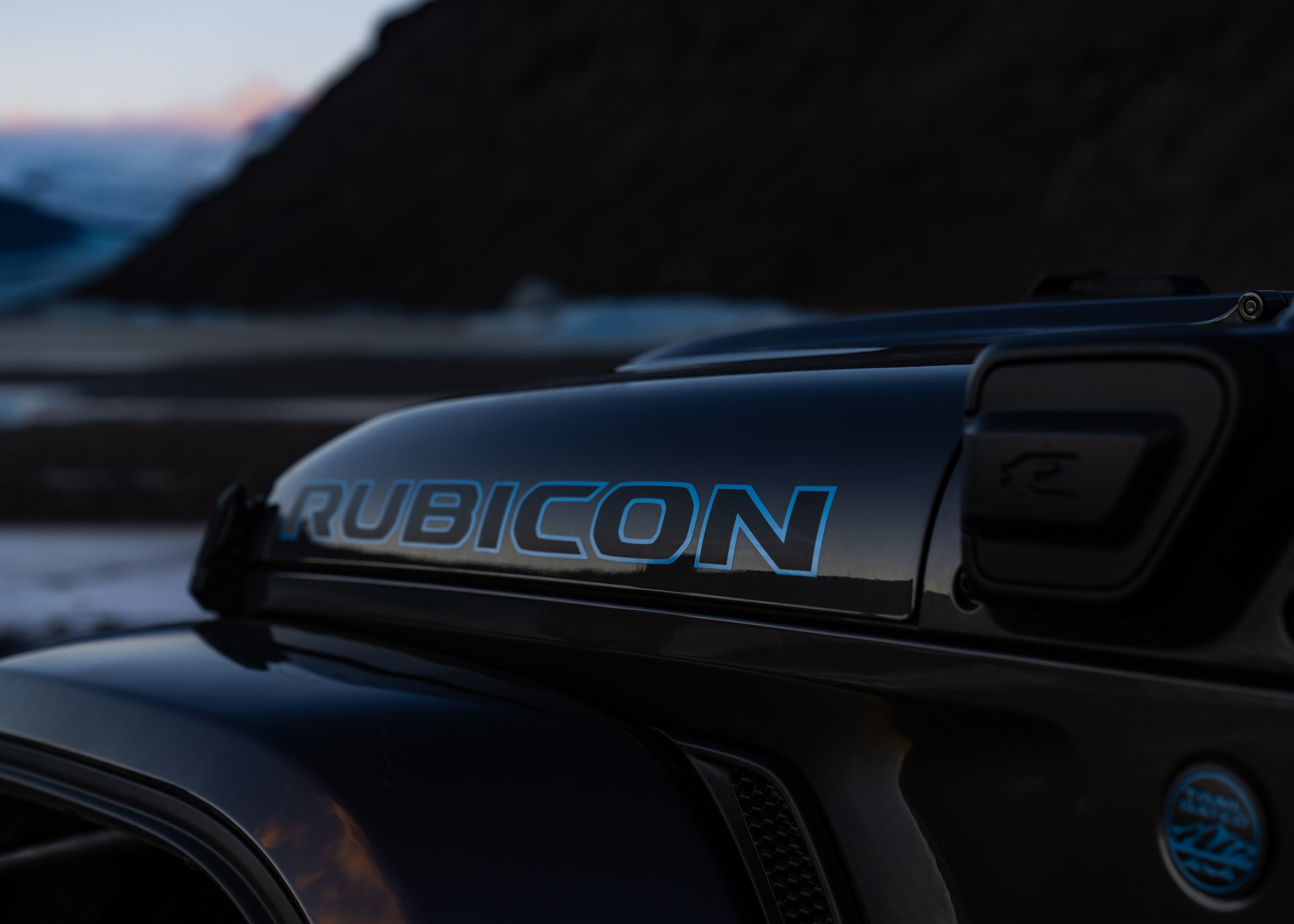 Jeep牧马人Rubicon引擎盖徽标特写，背景为海岸风光