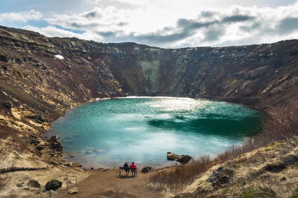 a couple of people are sitting on a bench next to a lake .