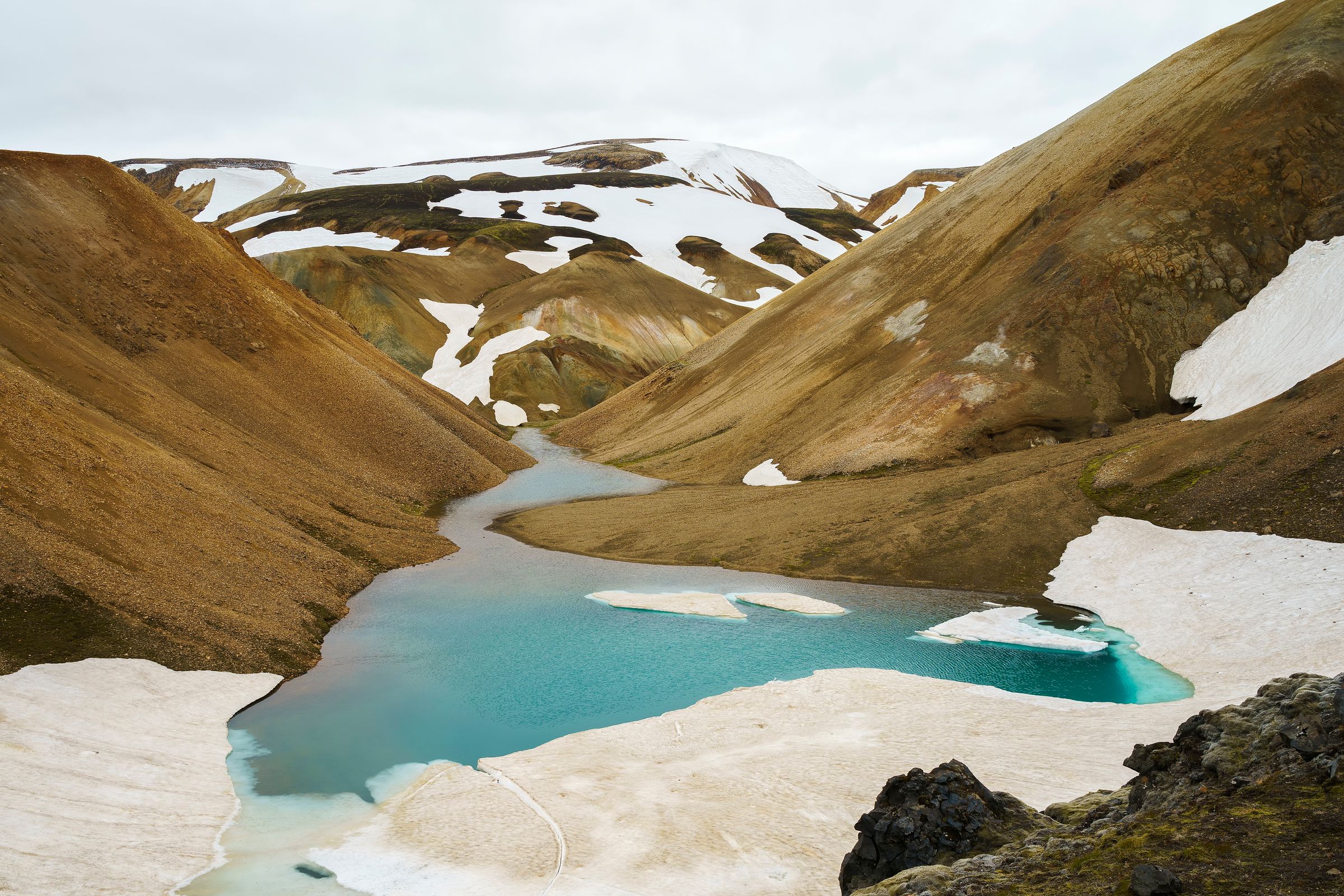 un río fluyendo a través de un valle rodeado por montañas cubiertas de nieve.