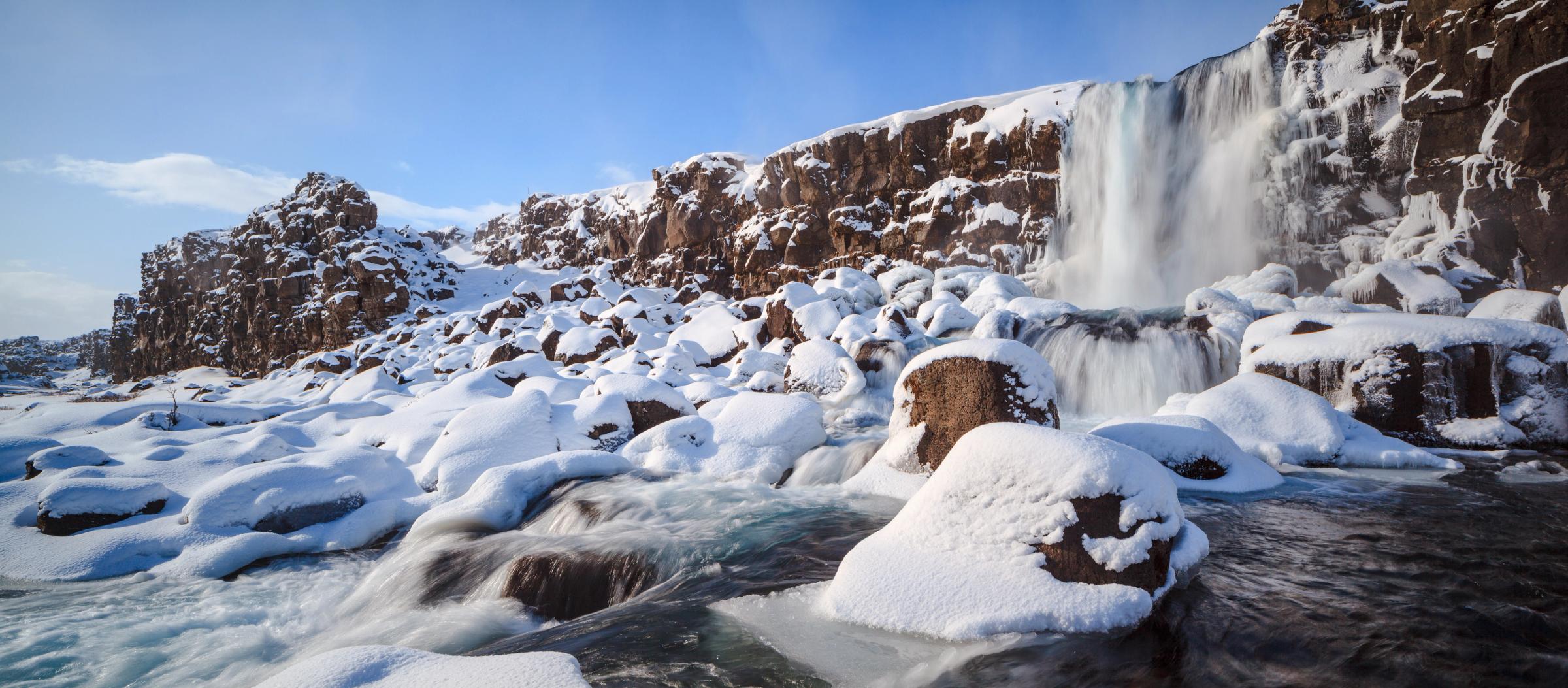 A waterfall descends into a snowy landscape with rocks and flowing water.