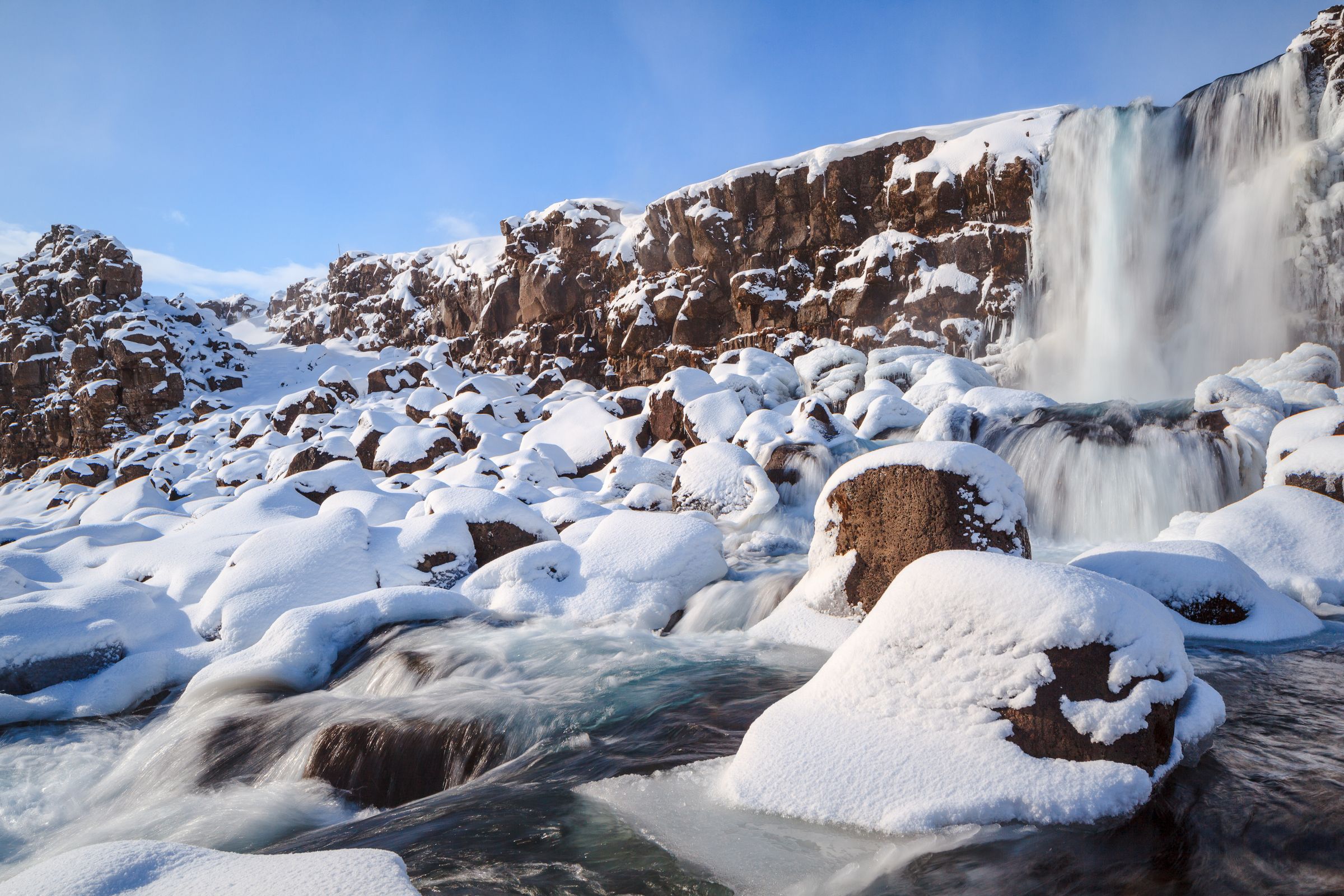 A waterfall descends into a snowy landscape with rocks and flowing water.