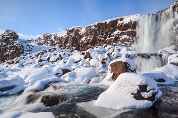 A waterfall descends into a snowy landscape with rocks and flowing water.