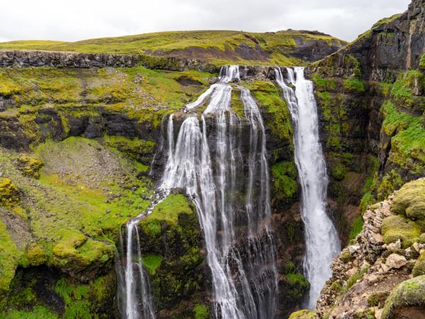 Multiple waterfalls cascade down a lush green, rocky canyon.
