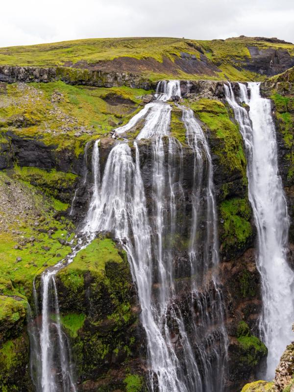 Multiple waterfalls cascade down a lush green canyon.