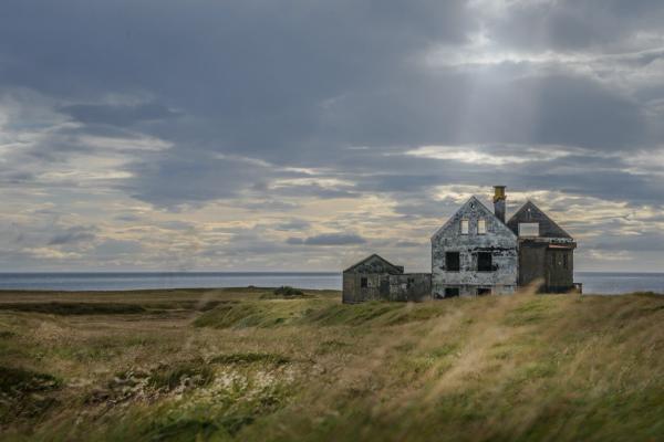 an old abandoned house is sitting in the middle of a field next to the ocean in north iceland.