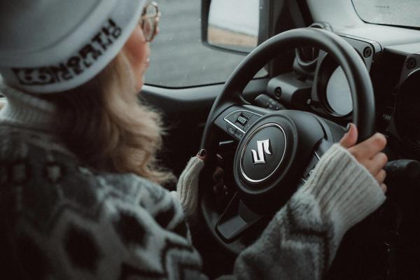 Person driving a Suzuki car, hands on the steering wheel.