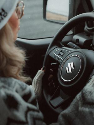 Person driving a Suzuki car, hands on the steering wheel.