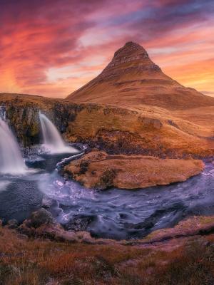 a waterfall with a mountain in the background at sunset and midnight sun in iceland.