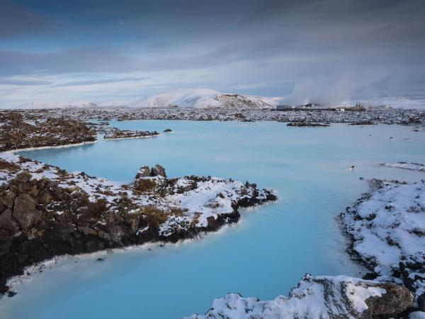 Light blue geothermal pools surrounded by snow-covered volcanic rocks, with steam rising in the distance.