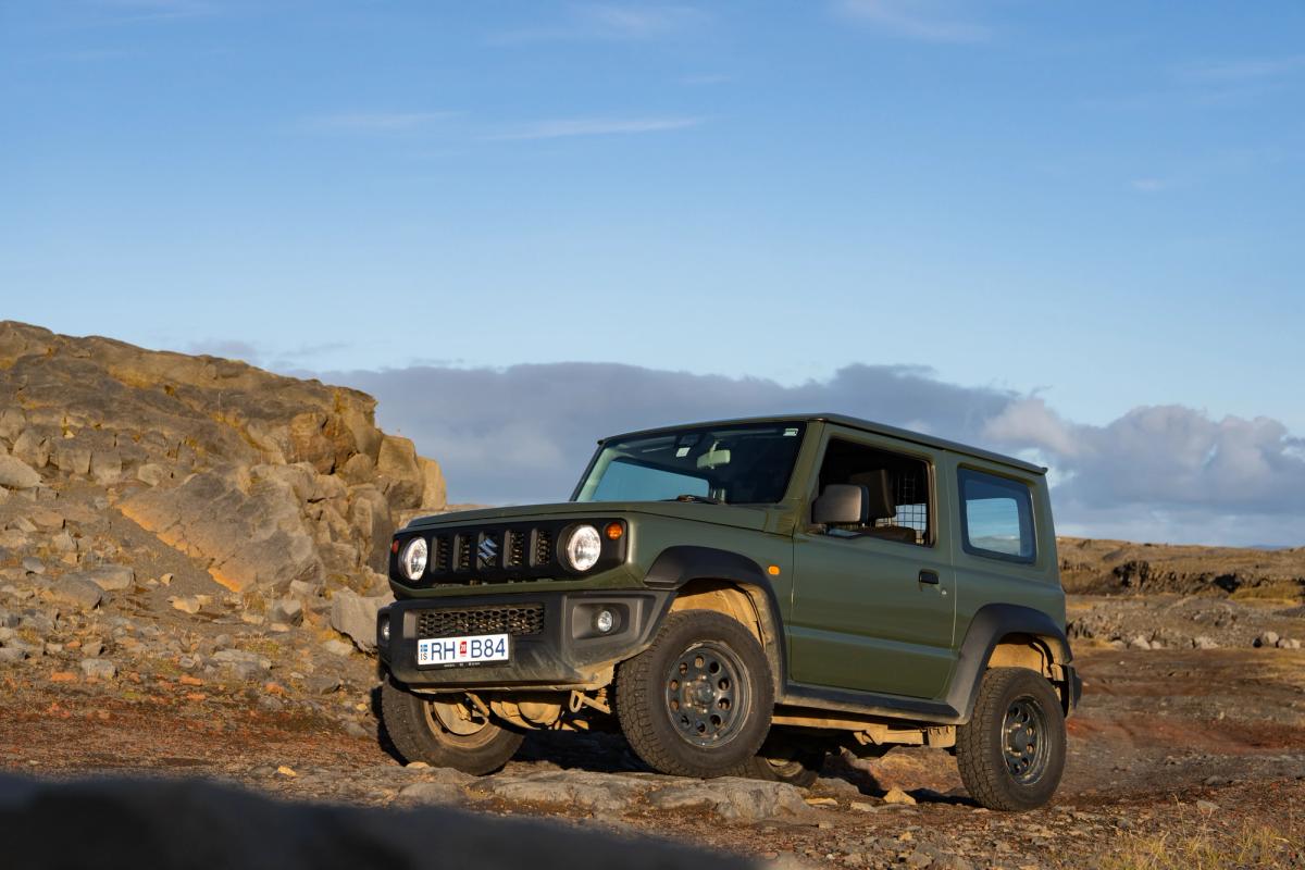 Suzuki Jimny mit Schaltgetriebe in schräger Frontansicht, auf felsigem Untergrund neben einem Felsvorsprung geparkt