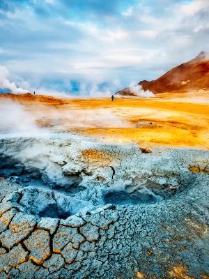 Steaming geothermal landscape with colorful, cracked earth.