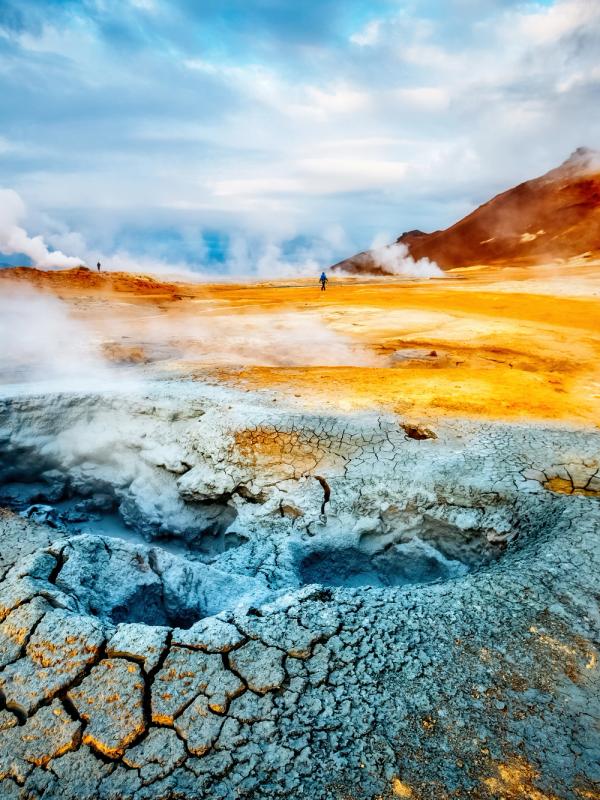 Steaming geothermal landscape with colorful, cracked earth.