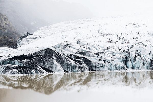a large snow covered glacier is reflected in a lake at höfn in Iceland.