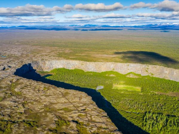 Vista aérea de un cañón profundo y arbolado que divide un paisaje rocoso y accidentado de una vasta llanura verde.