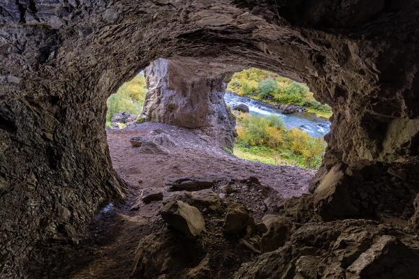 View from inside a cave framing a river and colorful autumn trees.