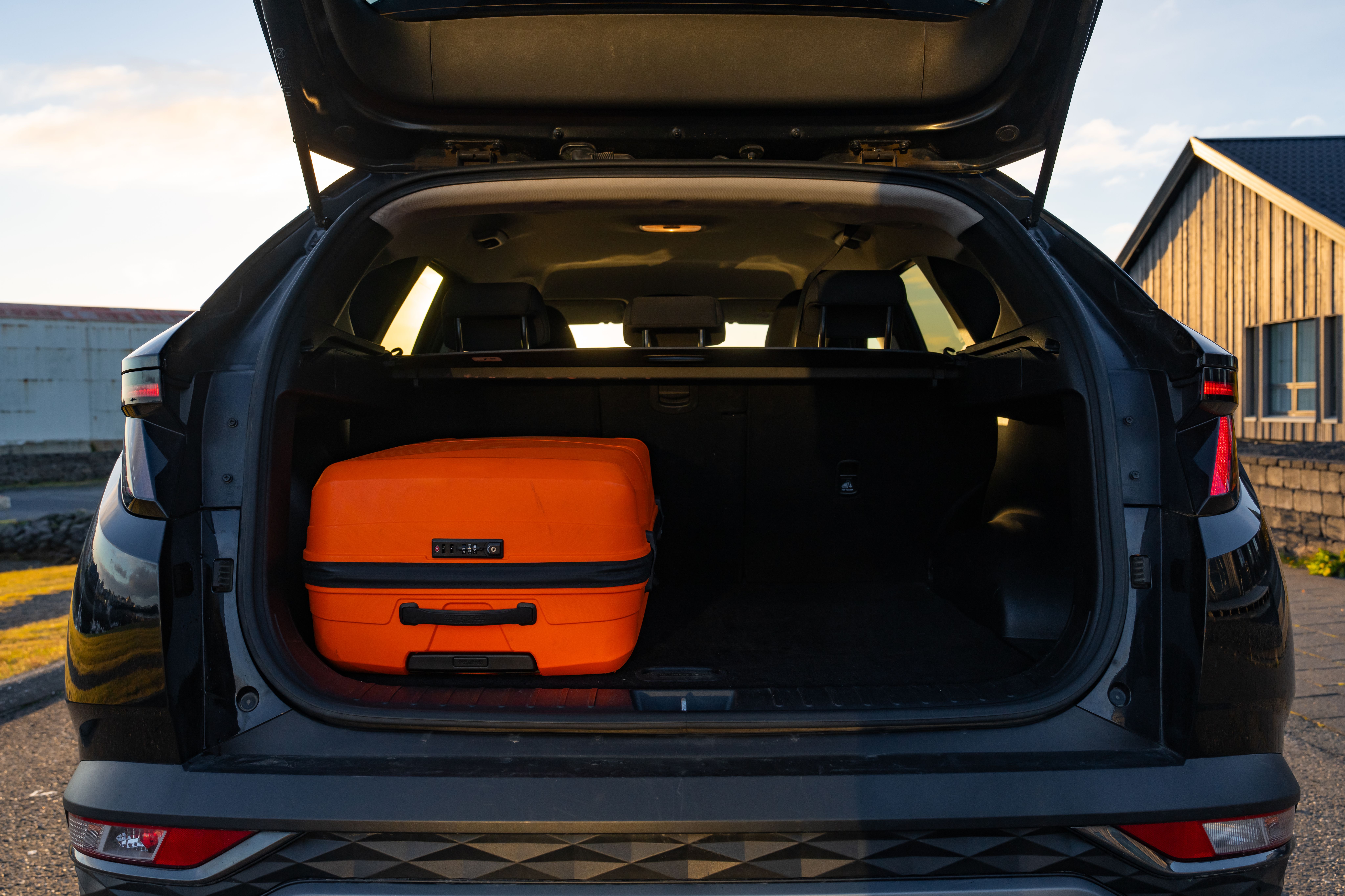 Open trunk of a dark SUV with an orange suitcase inside.