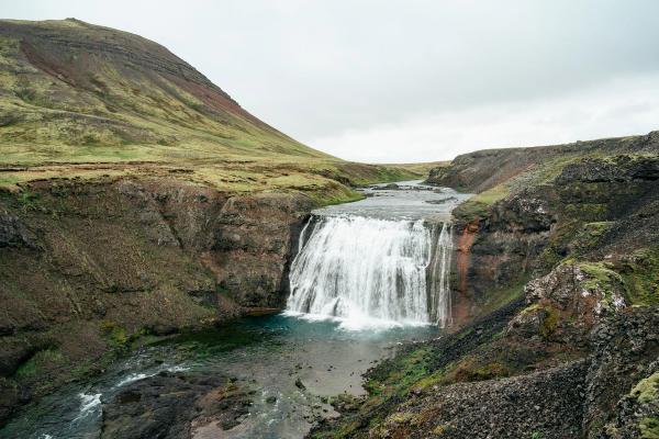 Waterfall in a rugged, green landscape under an overcast sky.