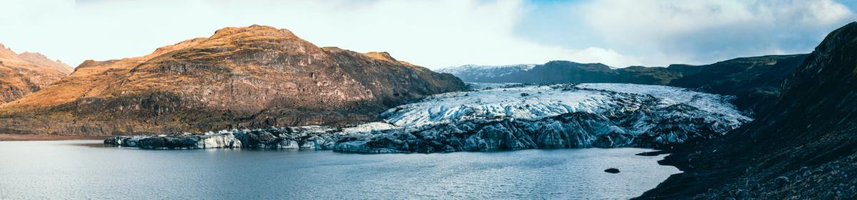 Panoramic view of a glacial lake with a large glacier and surrounding mountains.