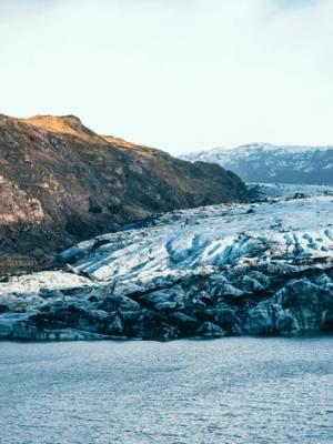 Panoramic view of a glacial lake with a large glacier and surrounding mountains.