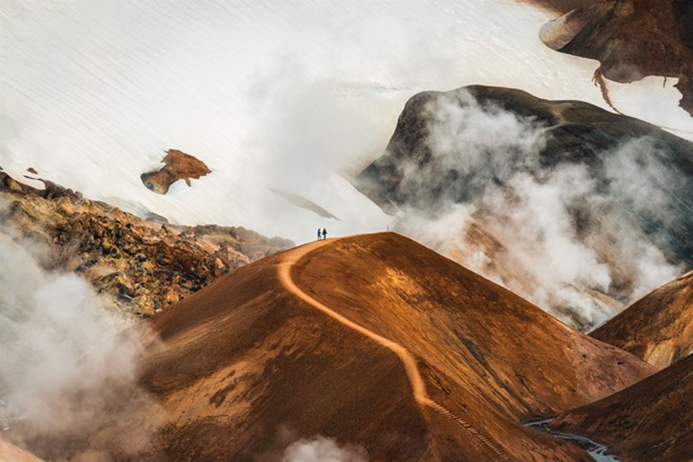a couple of people standing on top of a mountain surrounded by clouds at Hveradalir in iceland.