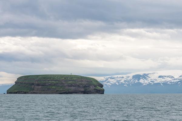 una pequeña isla en medio del océano con montañas en el fondo.