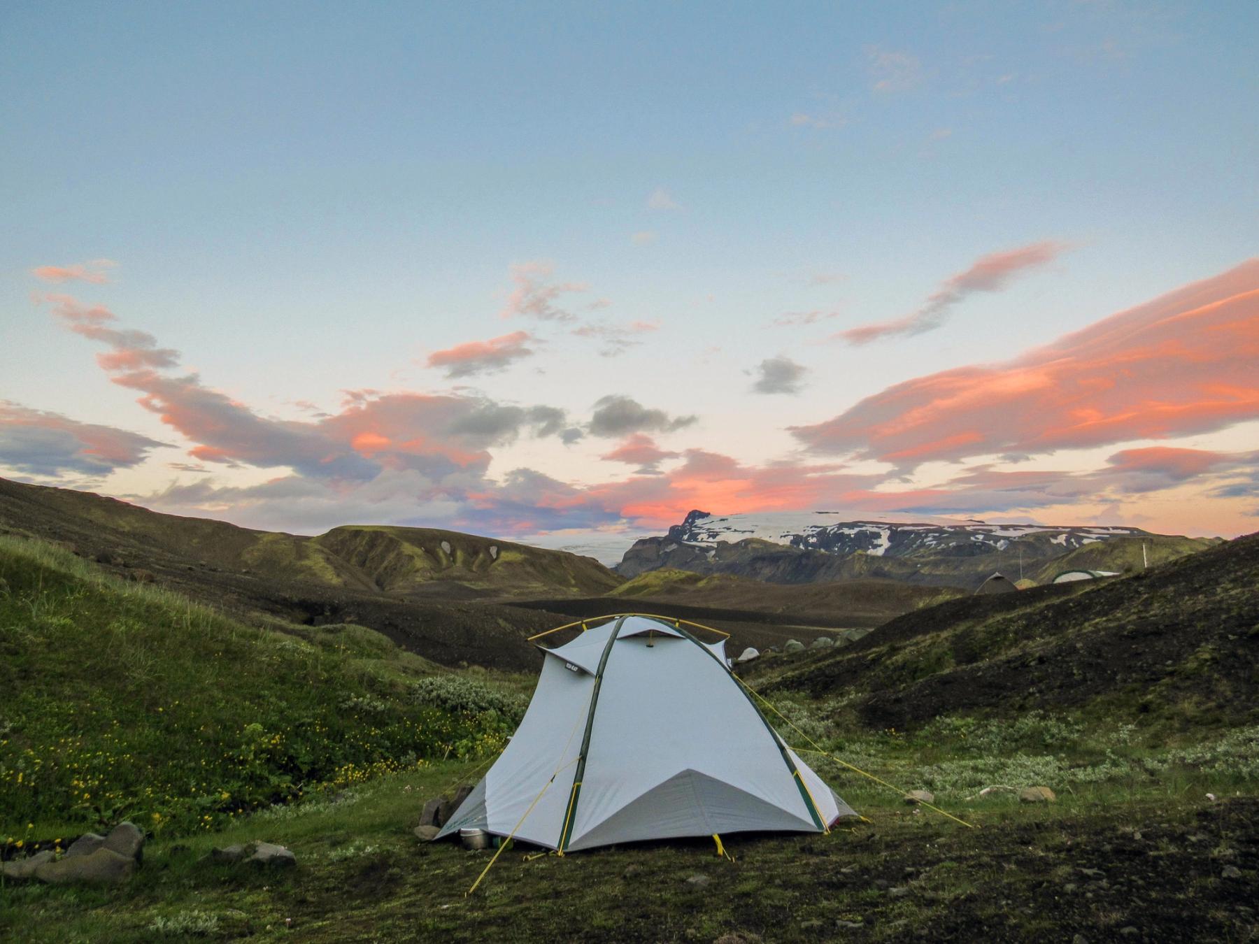 a tent is sitting in the middle of a field in the mountains at sunset .