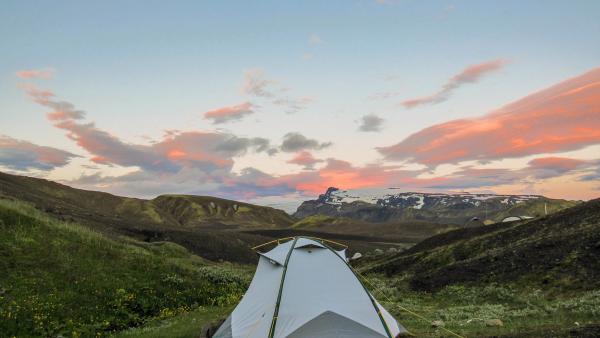 a tent is sitting in the middle of a field in the mountains at sunset .