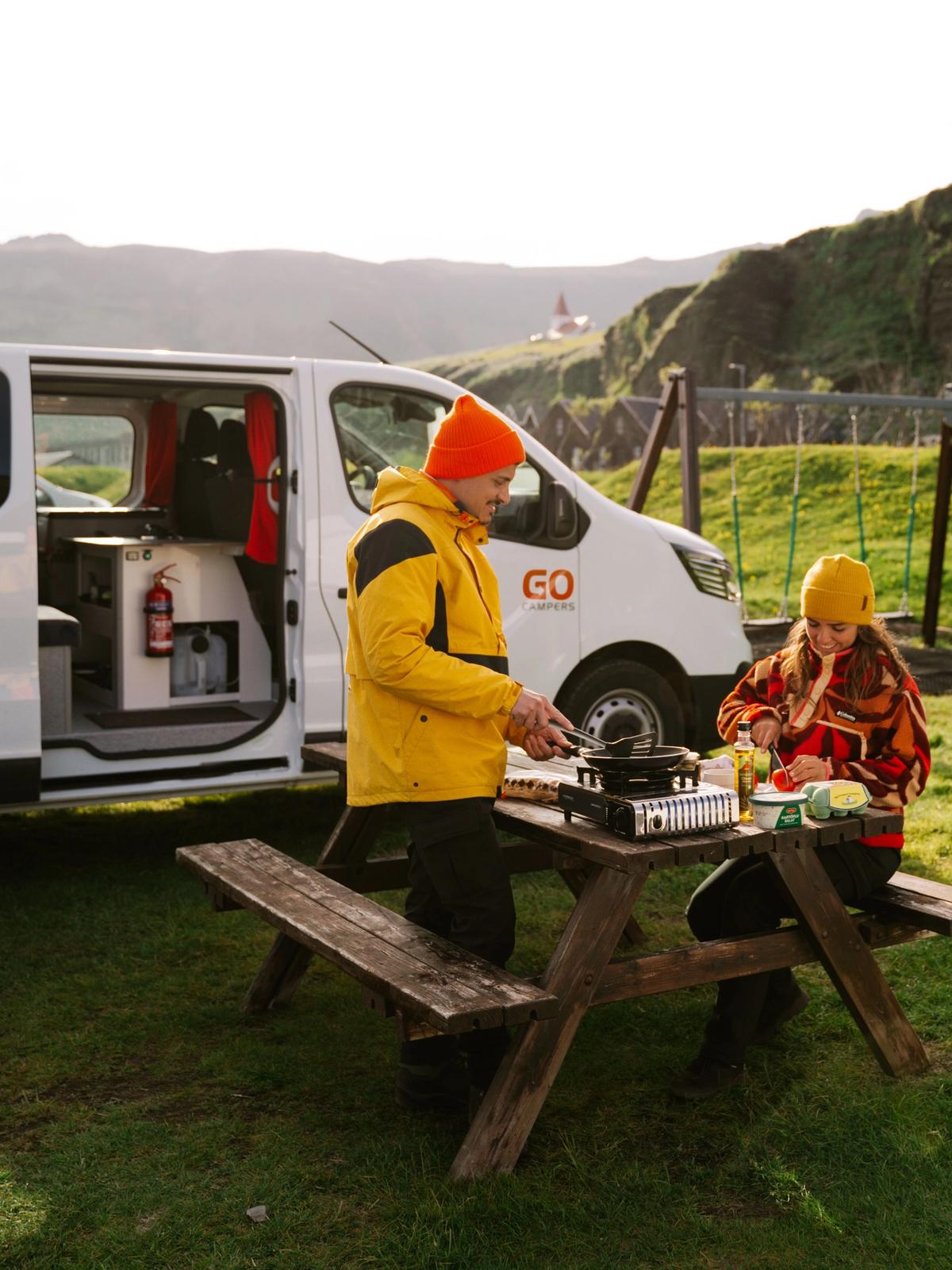 a woman is sitting on a blanket in a field next to a van .