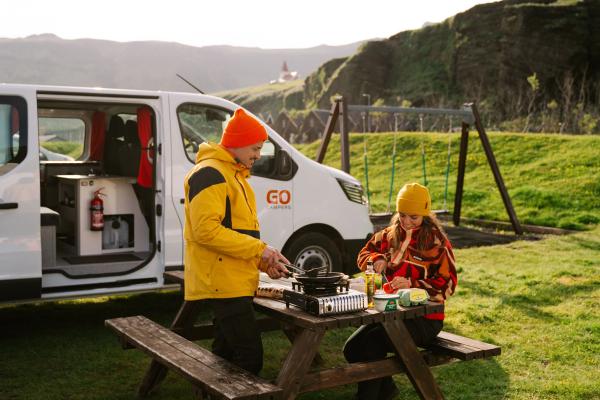 a man and a woman are sitting at a picnic table with a van in the background .